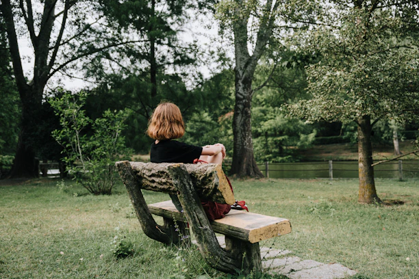 A thoughtful counselor speaking with a person sitting alone on a park bench.