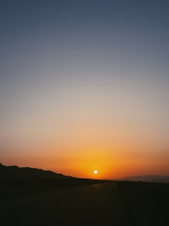 Sunset over a flat open land with distant mountains.