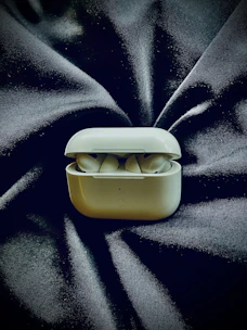 Wireless earbuds with a charging case placed on a soft fabric surface.