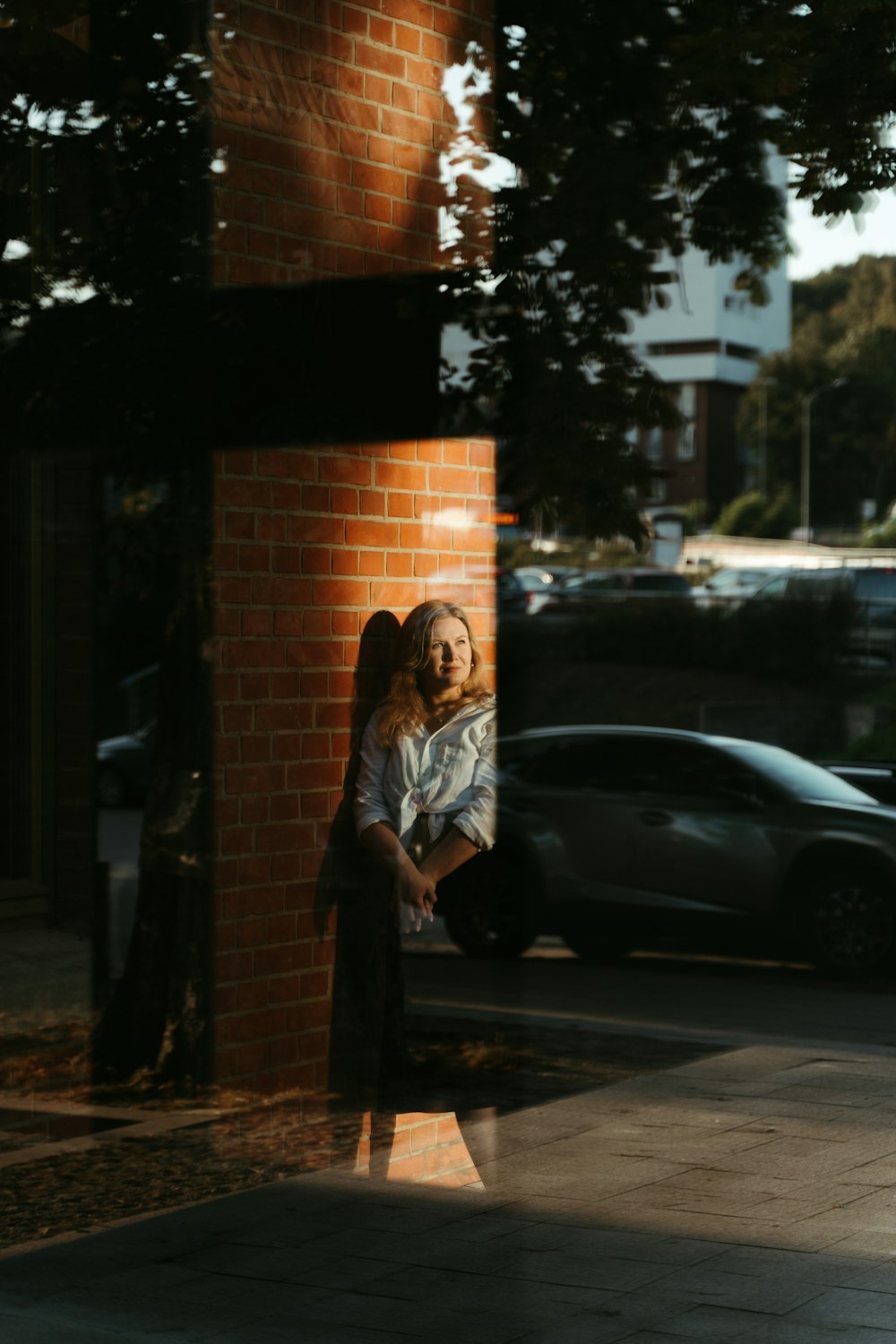 a woman leaning against a brick wall on a sidewalk