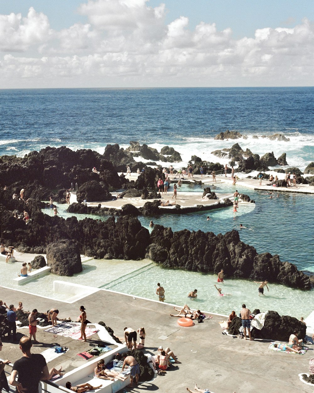 a group of people sitting around a pool next to the ocean