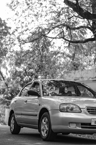 Smiling customer standing beside their freshly detailed silver sedan in a driveway.