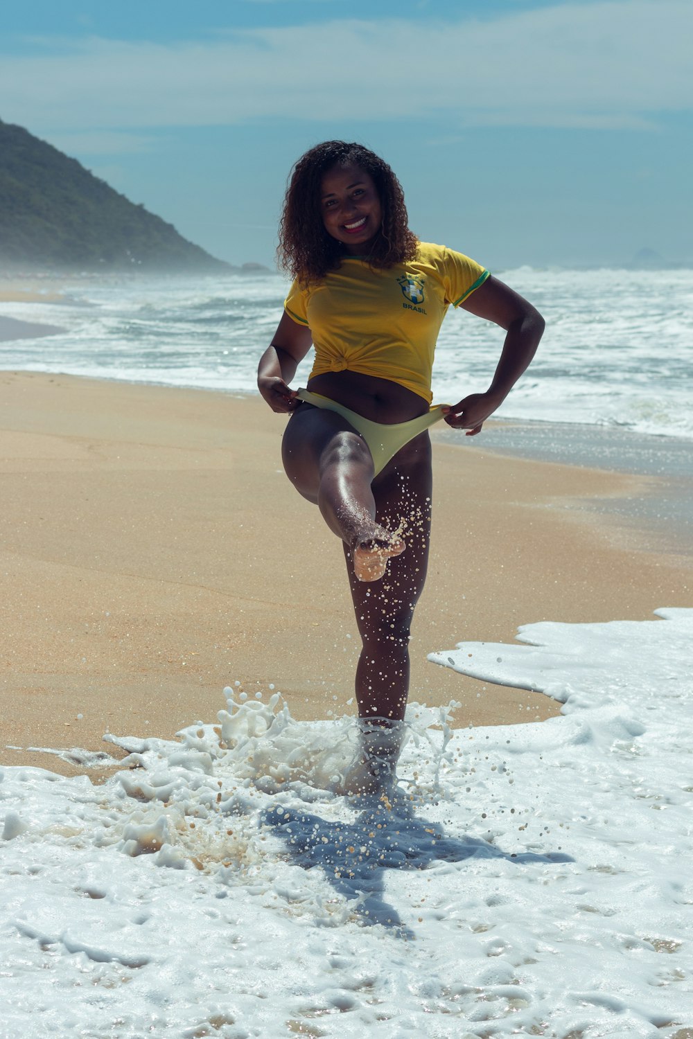 Une femme en chemise jaune se tient sur la plage