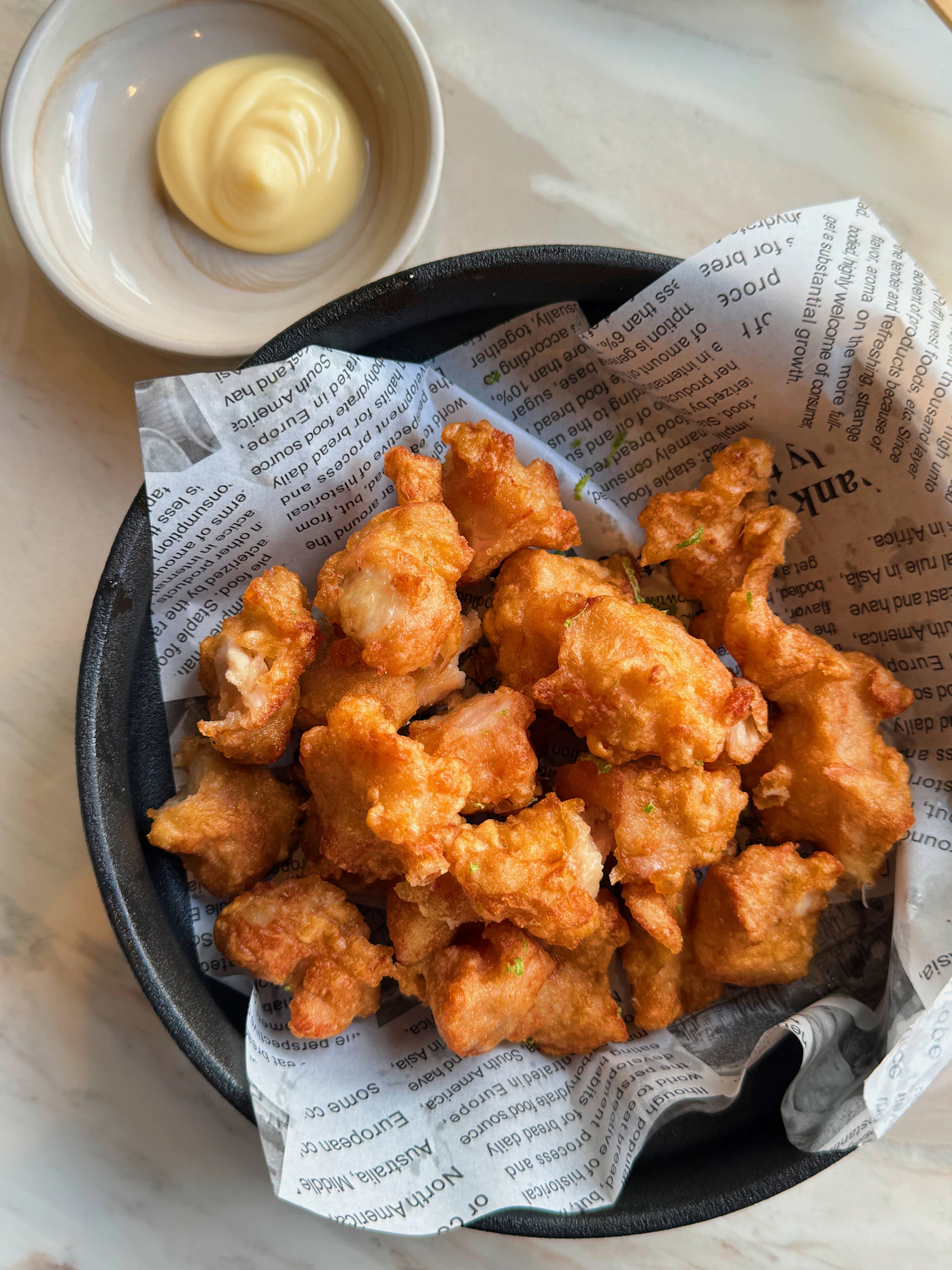 Bocconcini di pollo fritto croccante in una ciotola nera su carta da giornale, con salsa a fianco