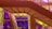 A modern staircase with a sleek design is positioned against a backdrop of colorful tinted glass panels. The vibrant hues of purple and yellow create an abstract effect with shadows and reflections.