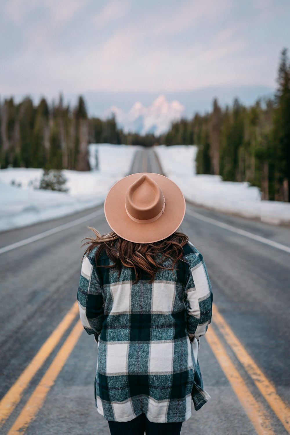 uma mulher com um chapéu parado na beira de uma estrada