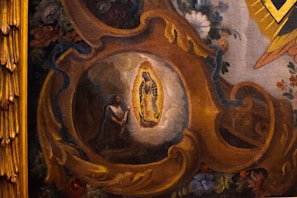 A detailed painting depicts a religious scene with a central figure illuminated by an intricate golden frame. Surrounding the figure are rich floral decorations and swirling ornate patterns in warm tones. The artwork conveys a sense of devotion and reverence.