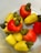 A collection of ripe and colorful cashew fruits, with a combination of yellow and red cashew apples, each topped with a green cashew nut. The fruits are placed together in a light-colored container, creating a vibrant contrast.