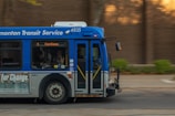 A public transit bus from the Edmonton Transit Service is captured in motion. The side of the bus shows advertisements and an electronic display indicates the destination as Capilano with route number 4. Inside, passengers are visible through the windows as they travel.