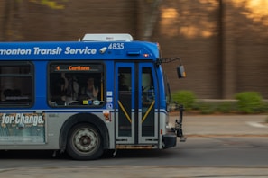 A public transit bus from the Edmonton Transit Service is captured in motion. The side of the bus shows advertisements and an electronic display indicates the destination as Capilano with route number 4. Inside, passengers are visible through the windows as they travel.
