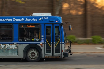 A public transit bus from the Edmonton Transit Service is captured in motion. The side of the bus shows advertisements and an electronic display indicates the destination as Capilano with route number 4. Inside, passengers are visible through the windows as they travel.