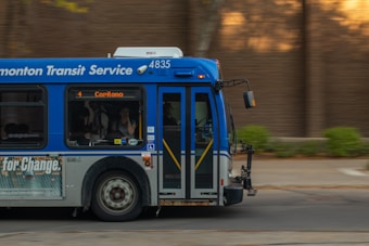 A public transit bus from the Edmonton Transit Service is captured in motion. The side of the bus shows advertisements and an electronic display indicates the destination as Capilano with route number 4. Inside, passengers are visible through the windows as they travel.