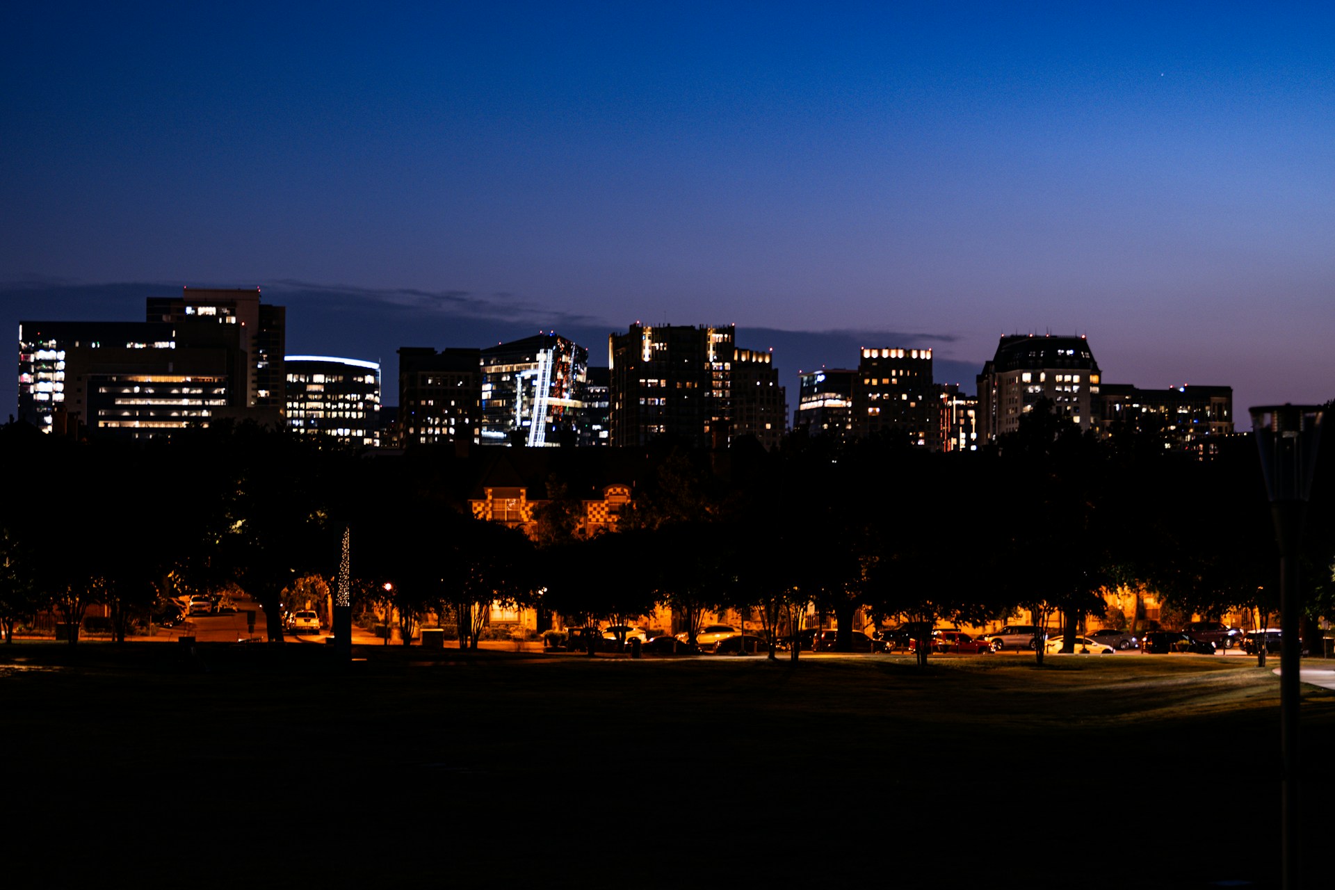 A vibrant cityscape at dusk with buildings illuminated, highlighting the contrast between urban life and the craftsmanship of the roofs.