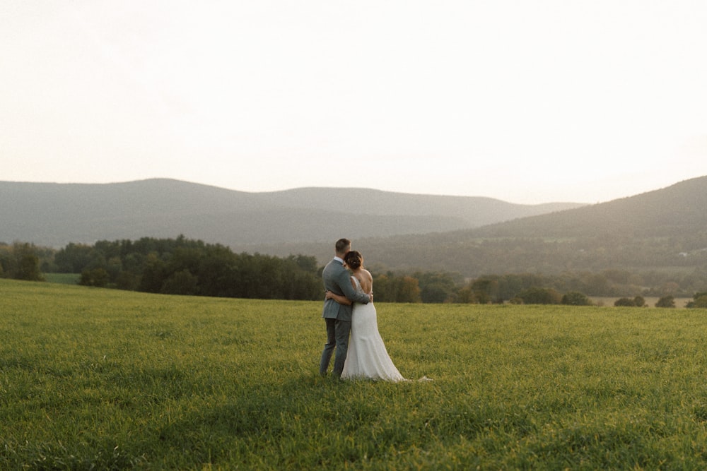 a bride and groom standing in a field with mountains in the background