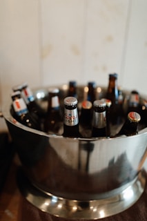 Several beer bottles with labeled caps are arranged in a metal ice bucket.