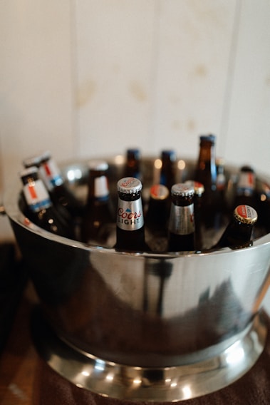 Several beer bottles with labeled caps are arranged in a metal ice bucket.