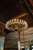 A rustic chandelier hanging in a warmly lit living room with wooden beams.
