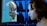A futuristic scene where a human-like robot face emerges from a computer screen, closely facing a woman with brown hair. The background consists of a grid of blue-lit panels.
