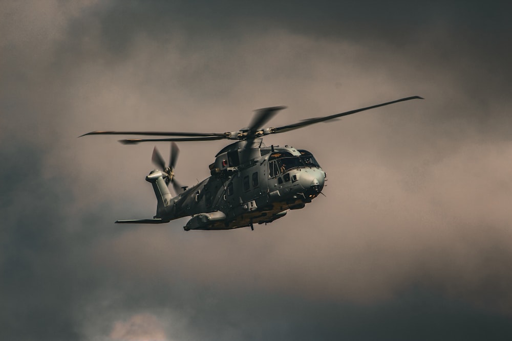 a military helicopter flying through a cloudy sky