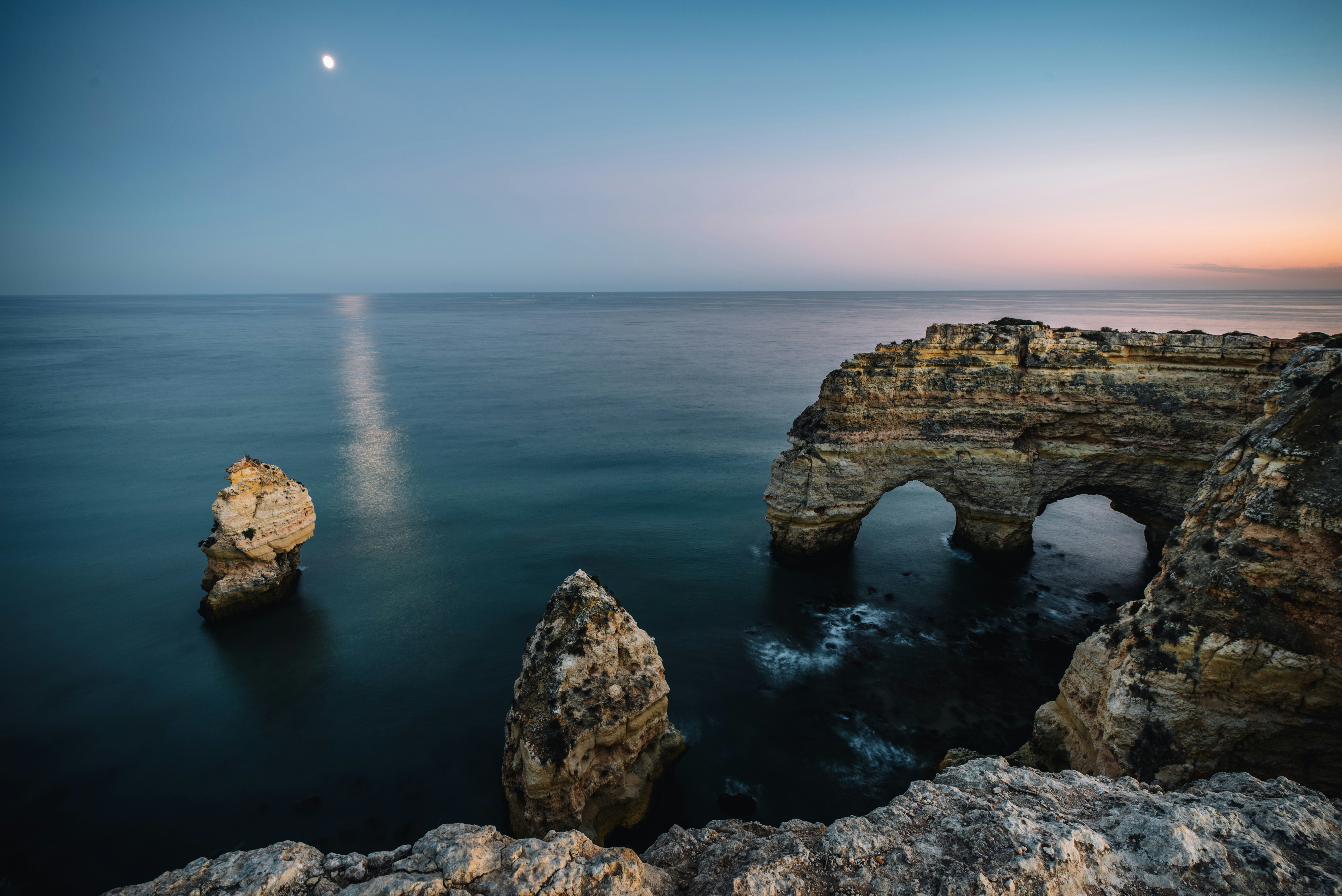 a rock formation in the ocean with a moon in the sky