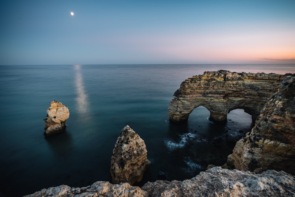 a rock formation in the ocean with a moon in the sky