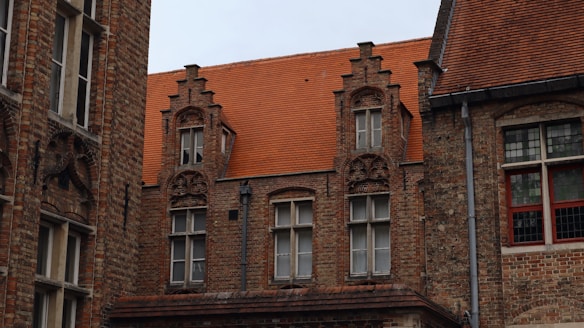 A historic brick building features ornate architectural details, including decorative gables and red-tiled roofing. The windows are tall with white frames, and there is a mix of older stained glass and newer panes.