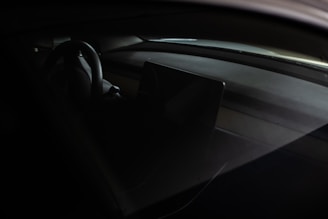 The interior of a car featuring a steering wheel and a dashboard with a central display screen. The lighting is dim, accentuating the sleek and modern design elements.