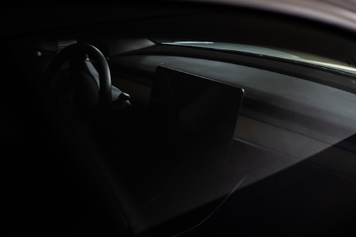 The interior of a car featuring a steering wheel and a dashboard with a central display screen. The lighting is dim, accentuating the sleek and modern design elements.