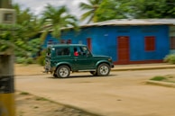 Green van driving through a leafy suburban neighborhood.
