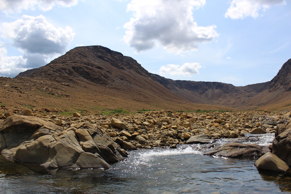 a stream running through a rocky valley with mountains in the background