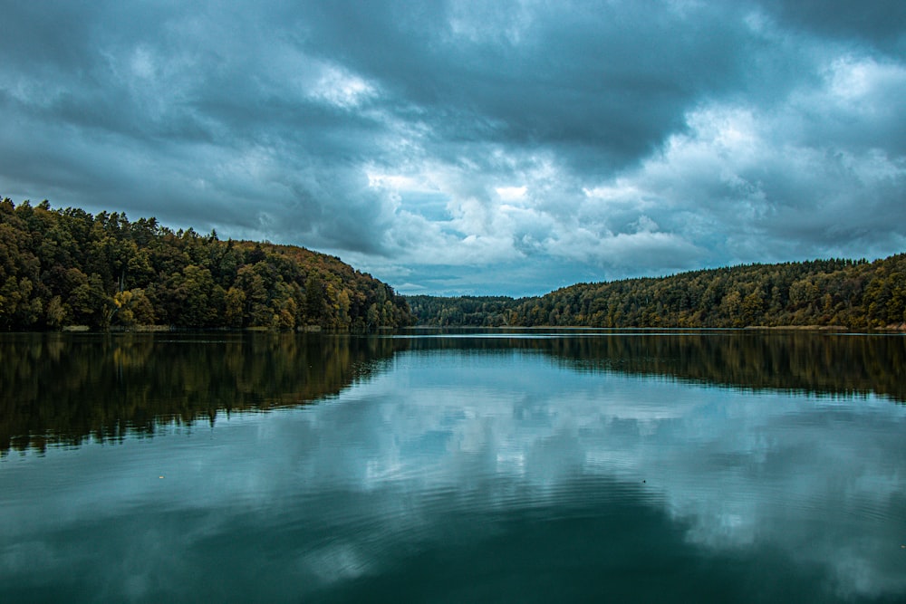 a body of water surrounded by forest under a cloudy sky