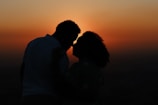Silhouetted couple embracing against a vibrant sunset backdrop, with warm orange and red tones filling the sky.