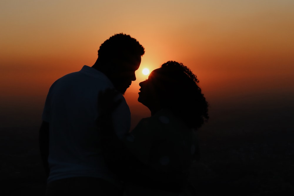 a man and a woman standing in front of a sunset