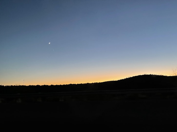 A serene sunset behind a silhouette of an astrologer studying ancient star charts.
