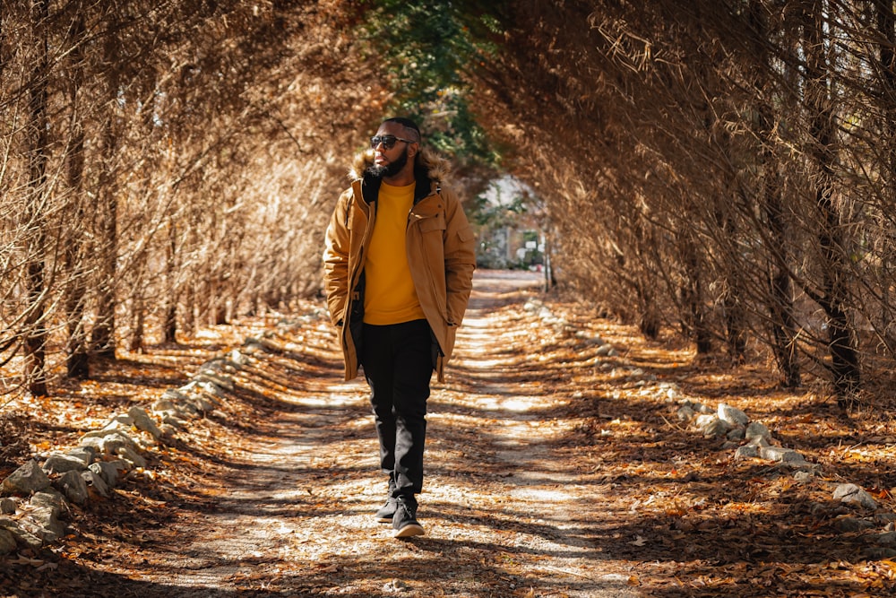 a man walking down a dirt road surrounded by trees