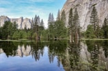 A serene mountain lake reflecting towering cliffs and pine trees.