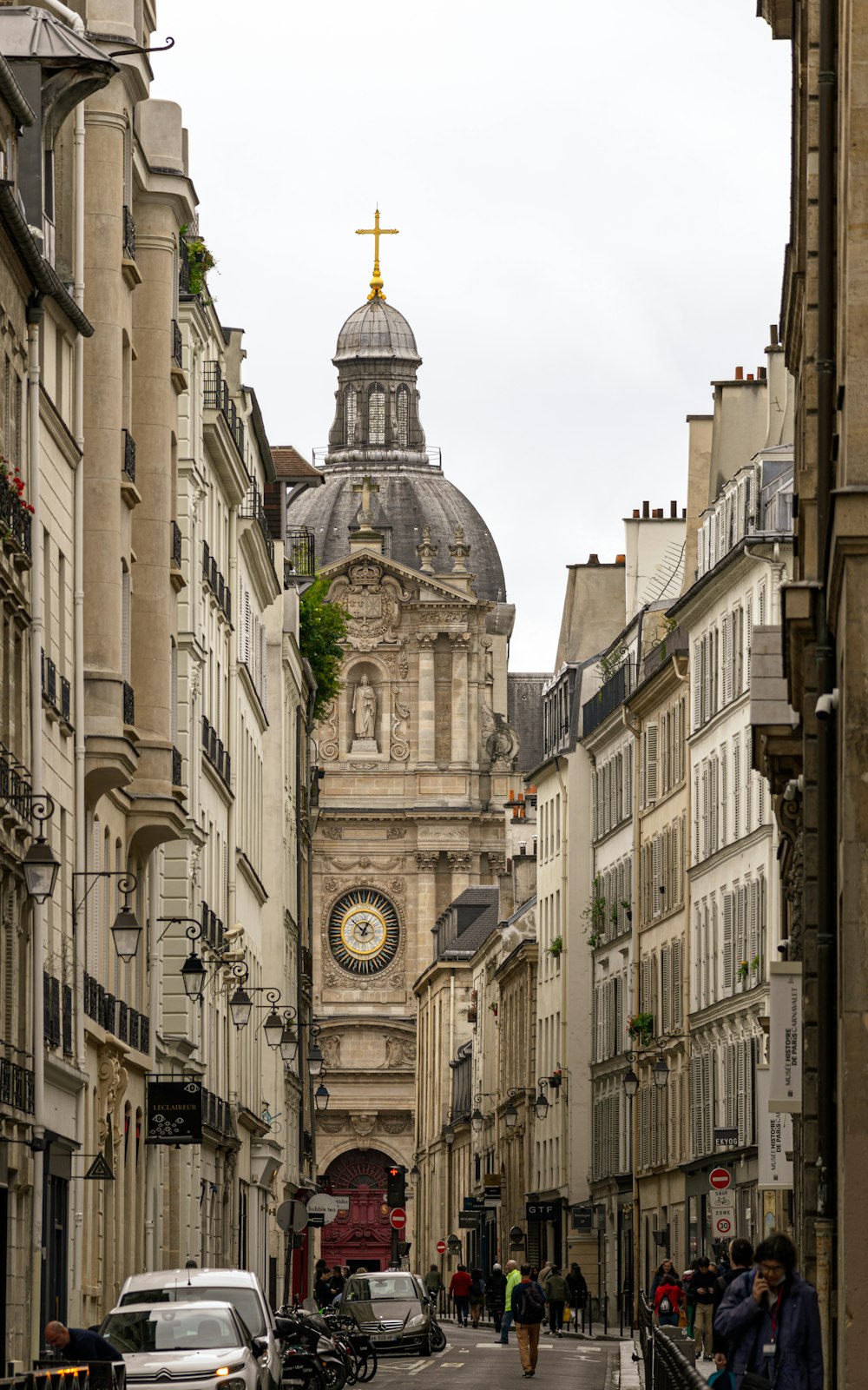 a narrow city street with a church steeple in the background