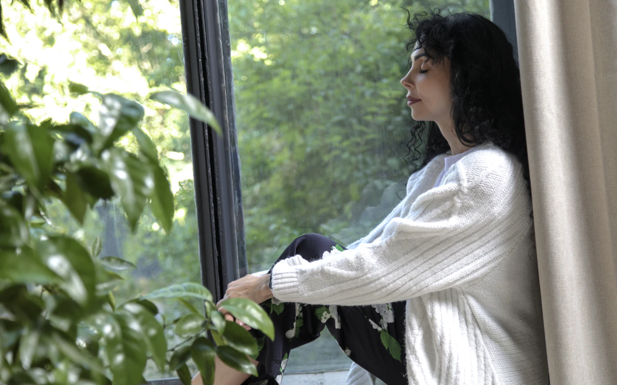 Frau sitzt ruhig am Fenster und nimmt sich eine Pause