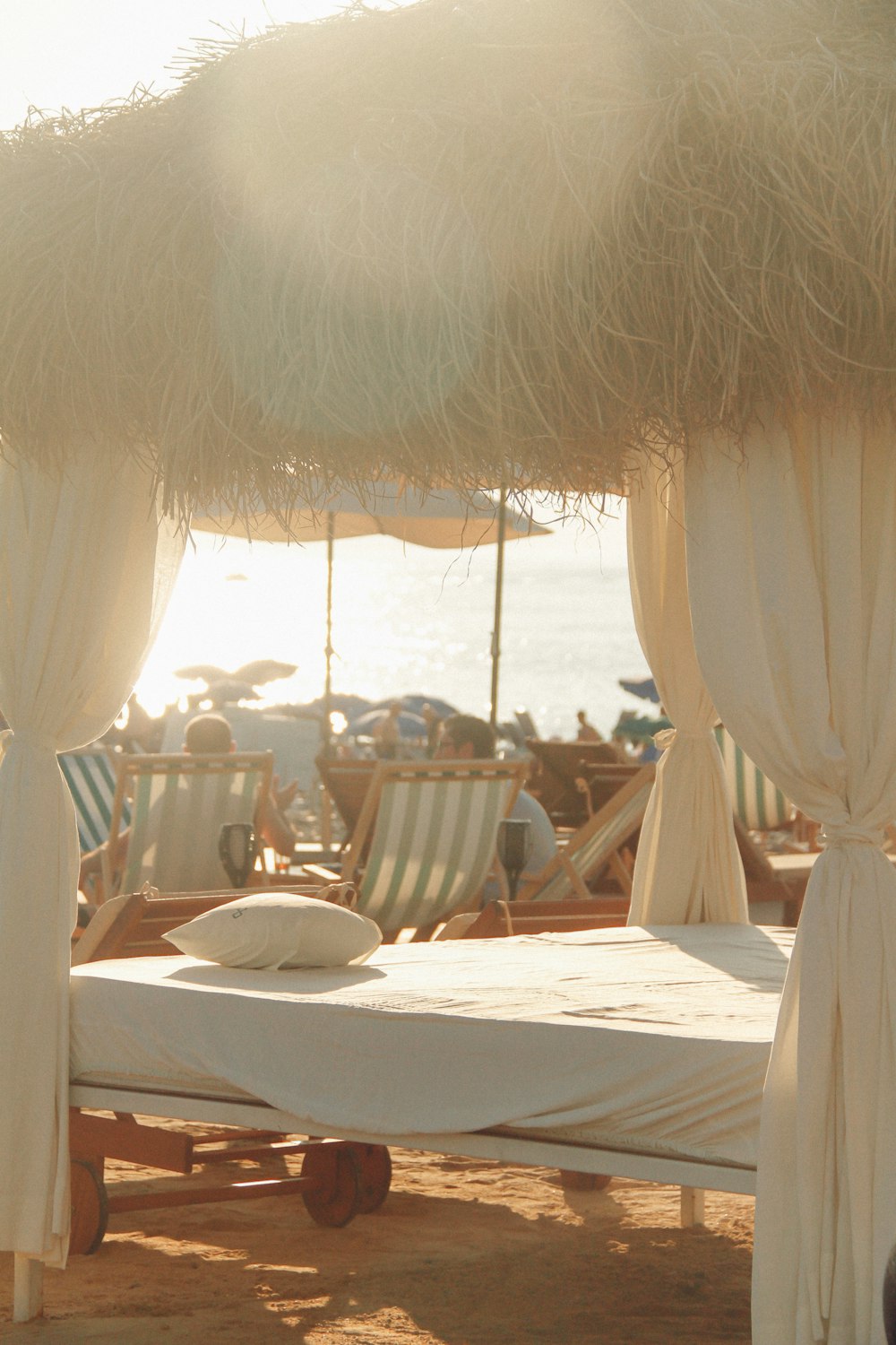a bed sitting under a thatched umbrella on a beach