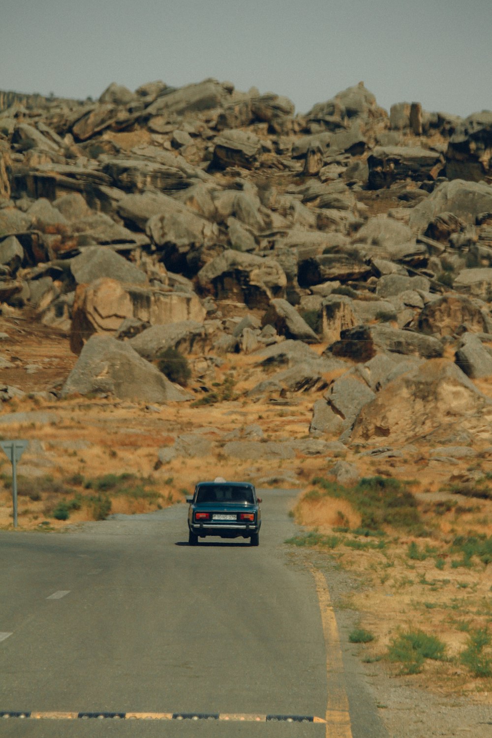 a car driving down a road in front of large rocks