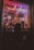 A dimly lit storefront window display features a large toy soldier surrounded by smaller toy soldiers. Neon lights in pink and purple cast a glow, with a sign overhead. The silhouette of a person looking into the window creates a mysterious vibe.