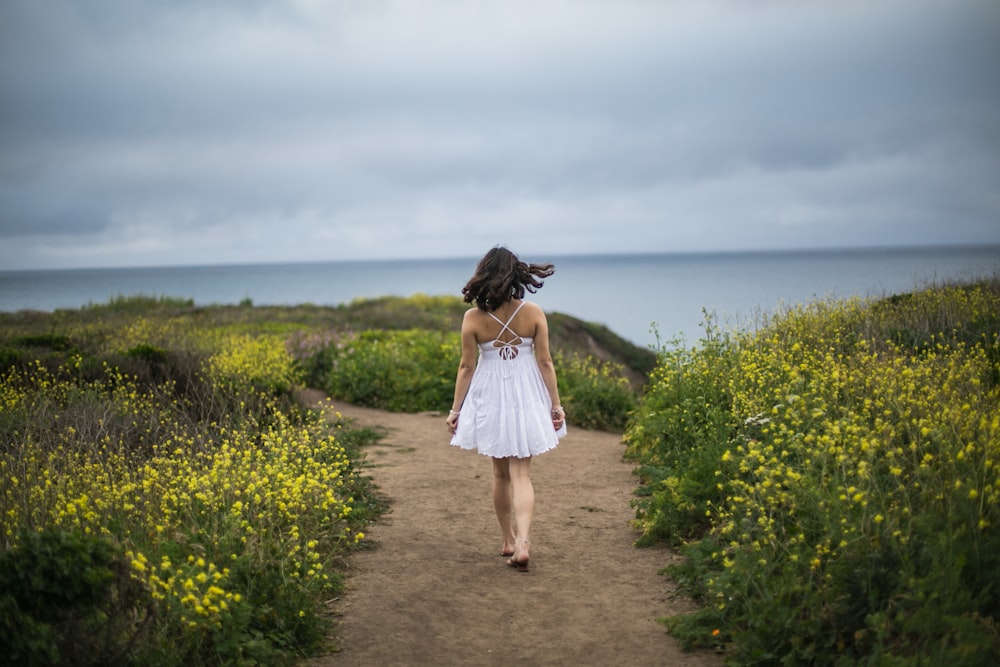 a woman in a white dress walking down a dirt path