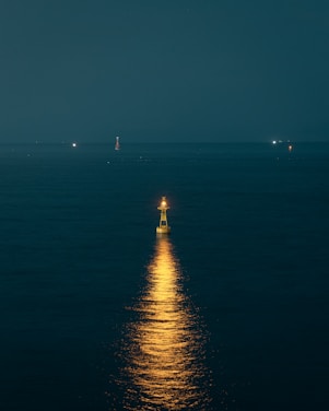 A calm lighthouse shining its light over a stormy sea at dusk.