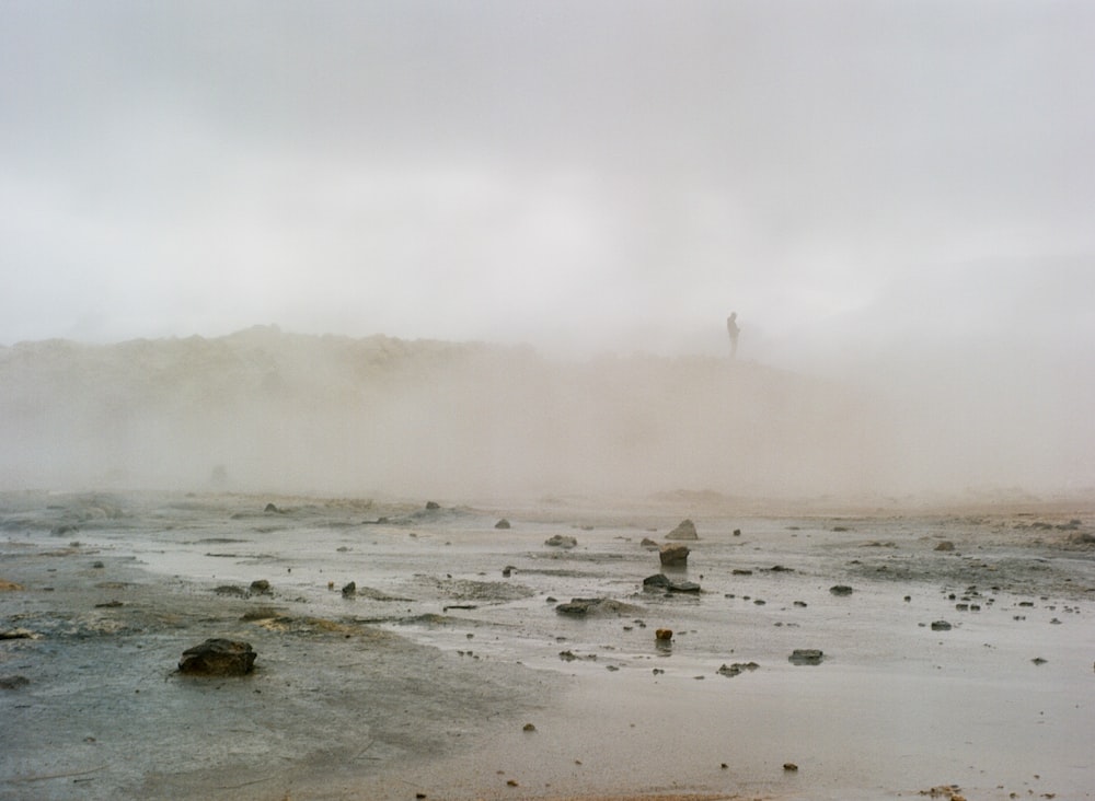 a foggy landscape with rocks and a person standing in the distance