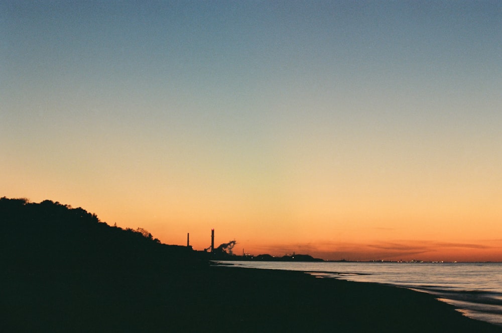 Una vista de una playa al atardecer con un faro en la distancia