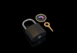 A brass padlock lies on a reflective black surface accompanied by a gold key attached to a circular keychain with colored segments.