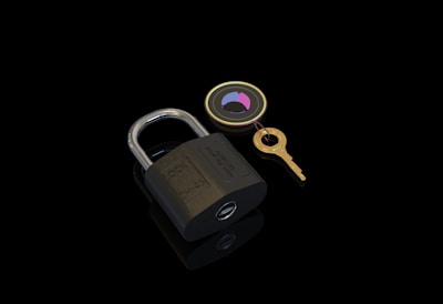 A brass padlock lies on a reflective black surface accompanied by a gold key attached to a circular keychain with colored segments.