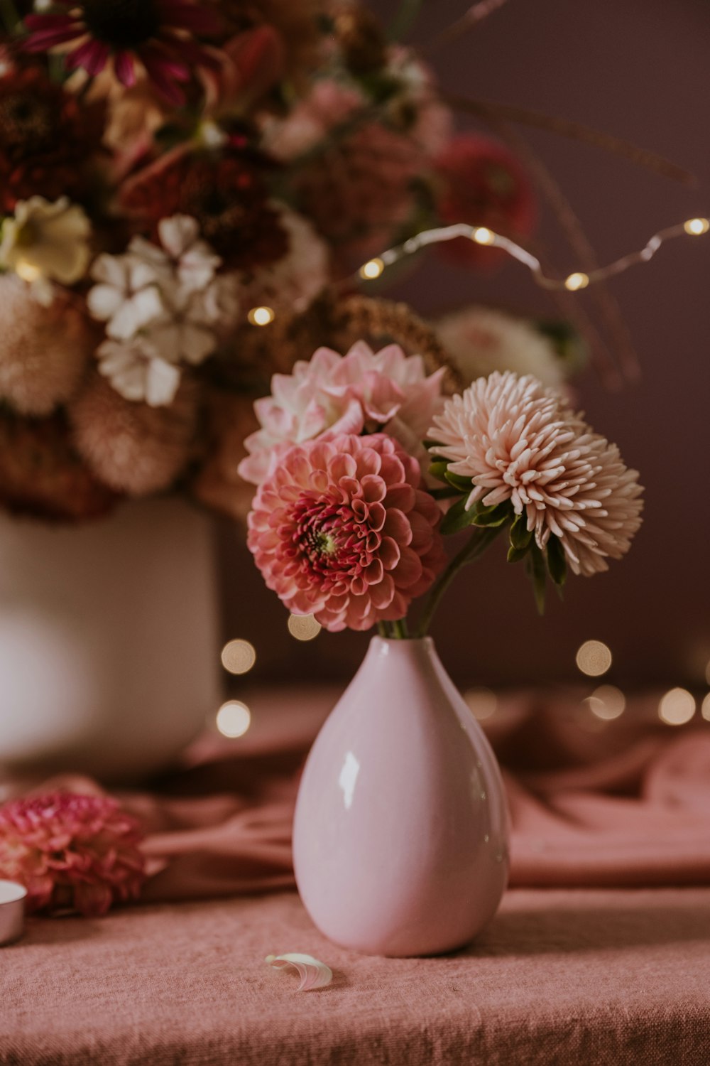 a white vase filled with pink flowers on top of a table