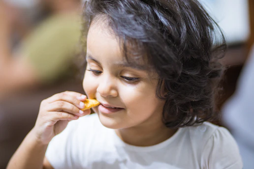 A joyful child holding a bowl of hot food, smiling in a sunlit community kitchen.