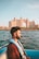 A person with a trimmed beard and wearing a life jacket sits in a boat. The background features the grand architecture of a large hotel or resort with an arch, possibly Atlantis The Palm in Dubai. The scene appears calm, with the gentle blue water surrounding the boat and a warm, late afternoon light illuminating the setting.